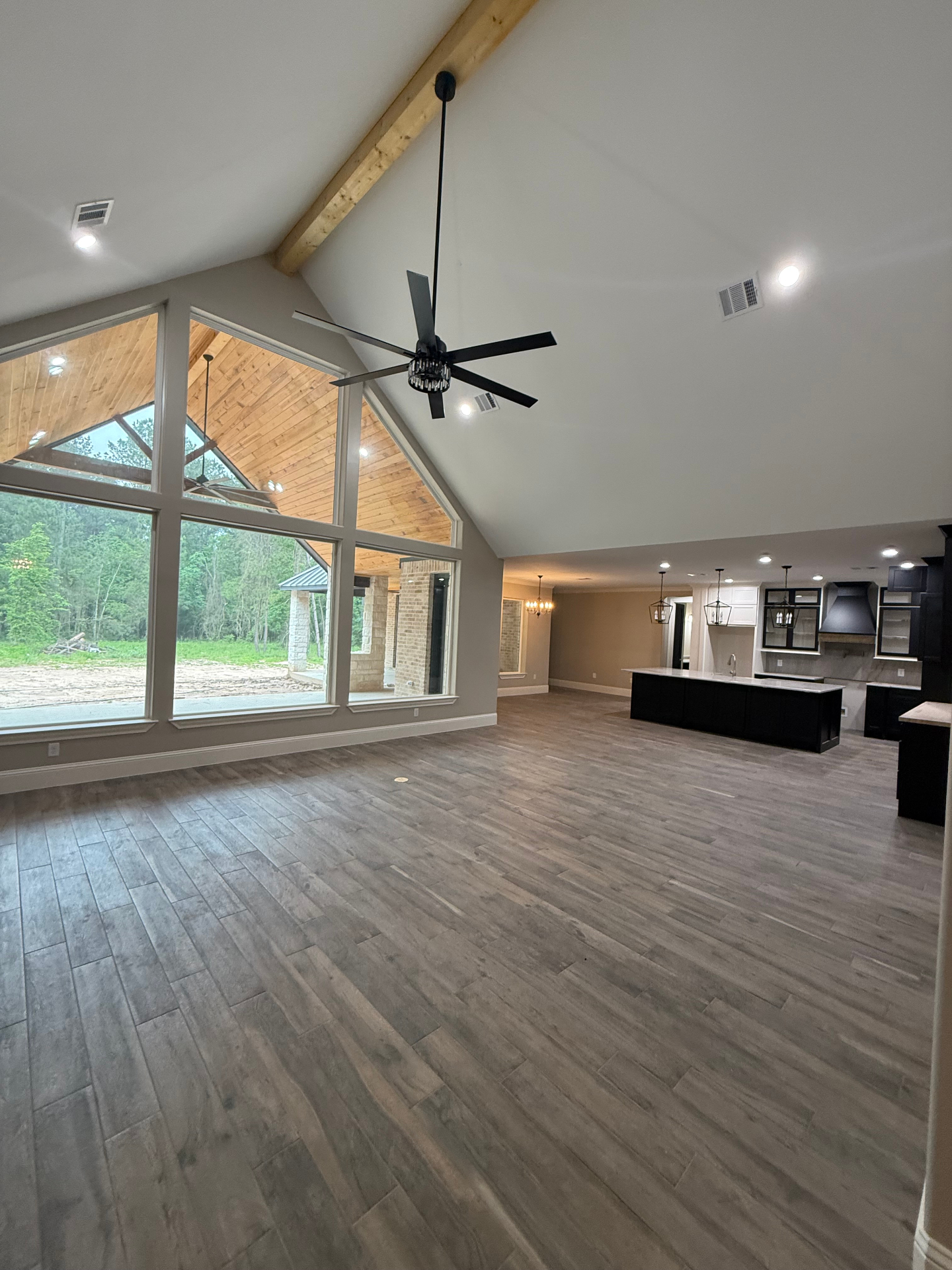 Vaulted open-concept living room with oversized windows and dark kitchen cabinetry